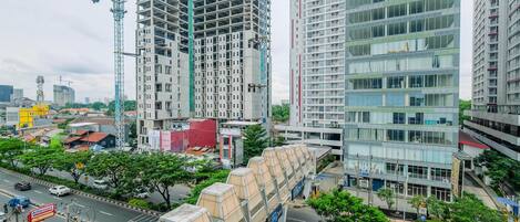 A high-rise building under construction with a crane, surrounded by other buildings and a busy street with vehicles and pedestrians.