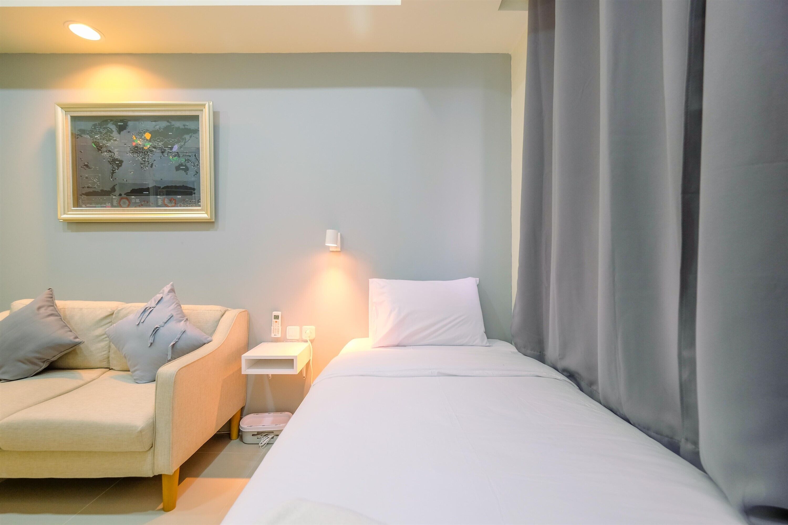Une chambre d’hôtel avec un lit, un canapé, une table de chevet, une lampe et une carte du monde encadrée accrochée au mur.