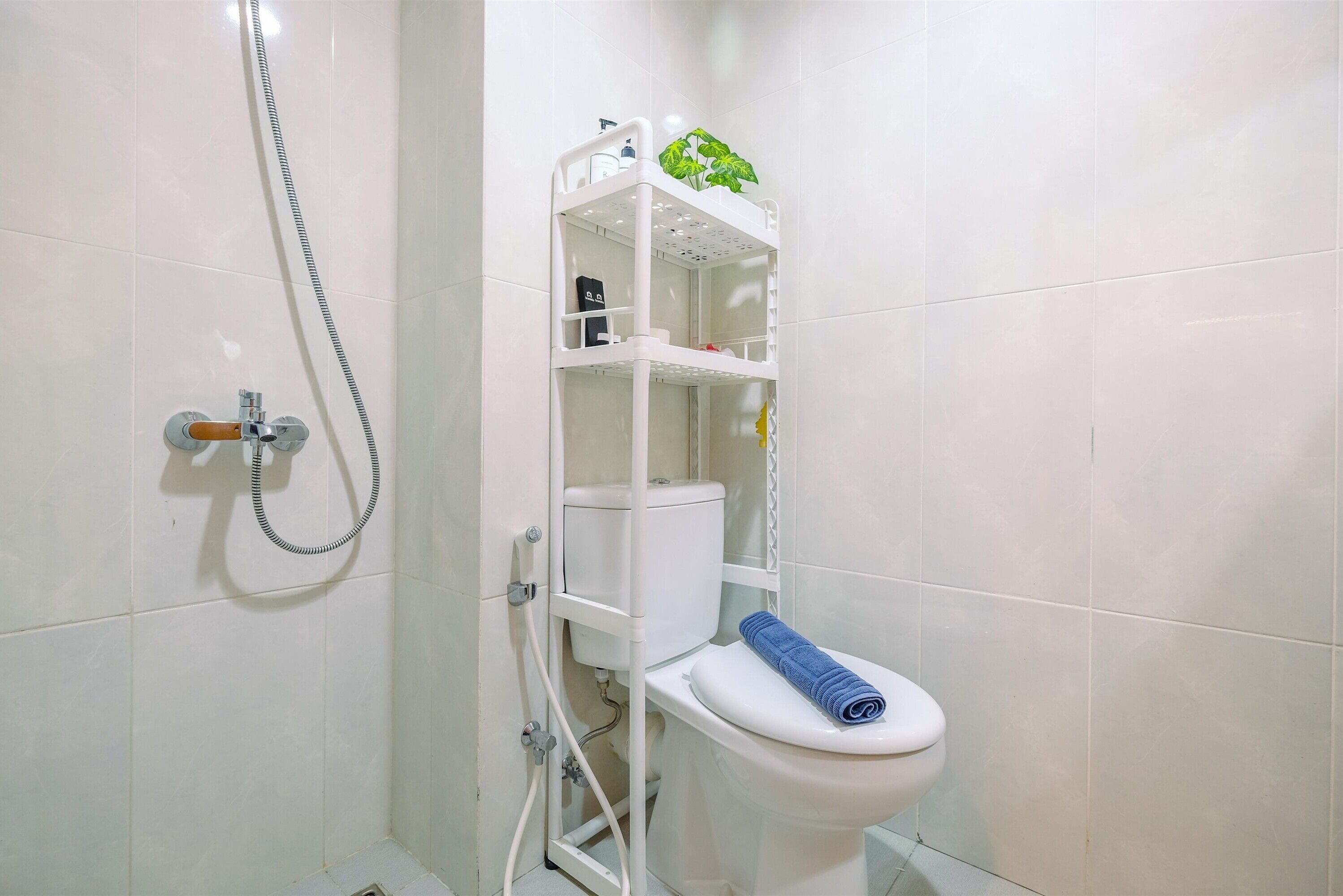 A compact bathroom with a white toilet, a shower enclosure, and a small shelf with toiletries.