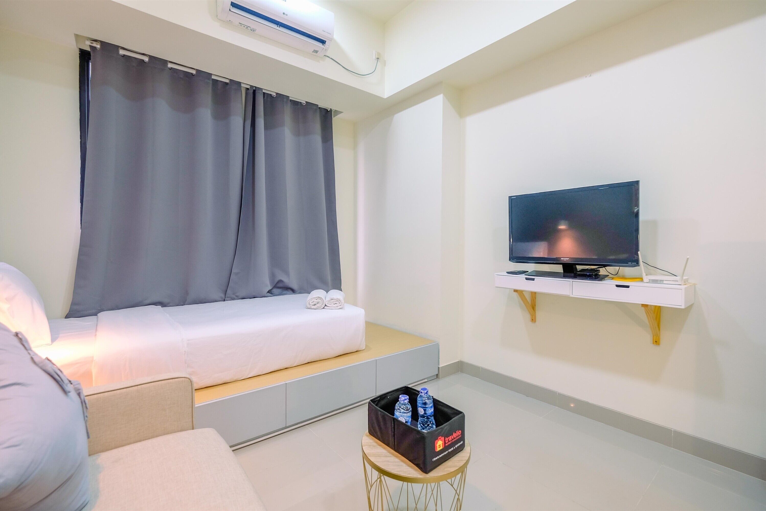 A hotel room with a bed, a TV on a shelf, and a small table with a water bottle.