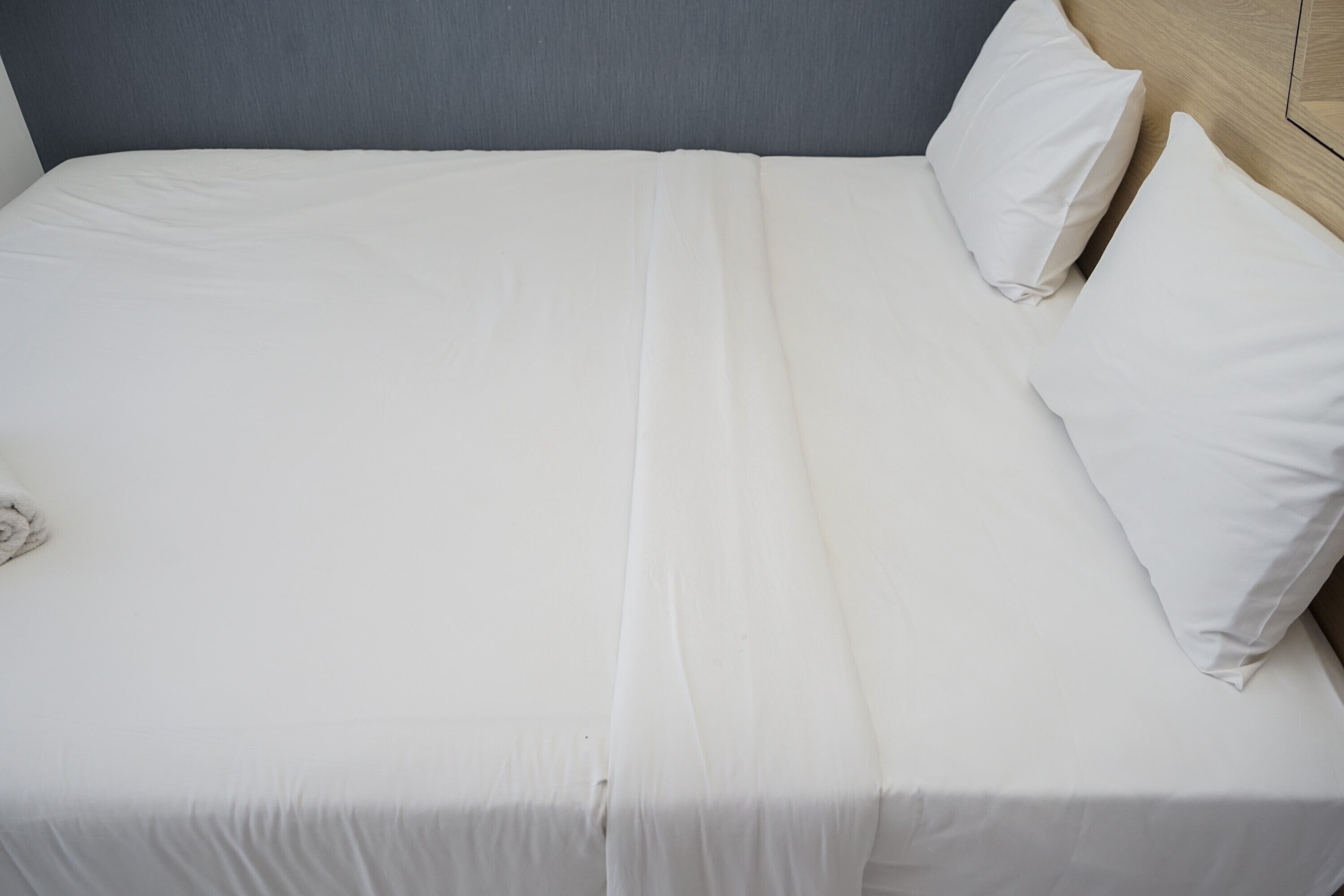 A neatly made bed with white linens and pillows, a grey headboard, and a wooden headboard on the right.