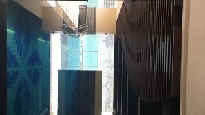 Un couloir étroit, avec une piscine d’un côté et un mur orné de motifs de l’autre.