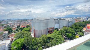 Un immeuble de grande hauteur à l’architecture moderne, entouré d’une végétation luxuriante et avec une vue sur le paysage urbain en arrière-plan.