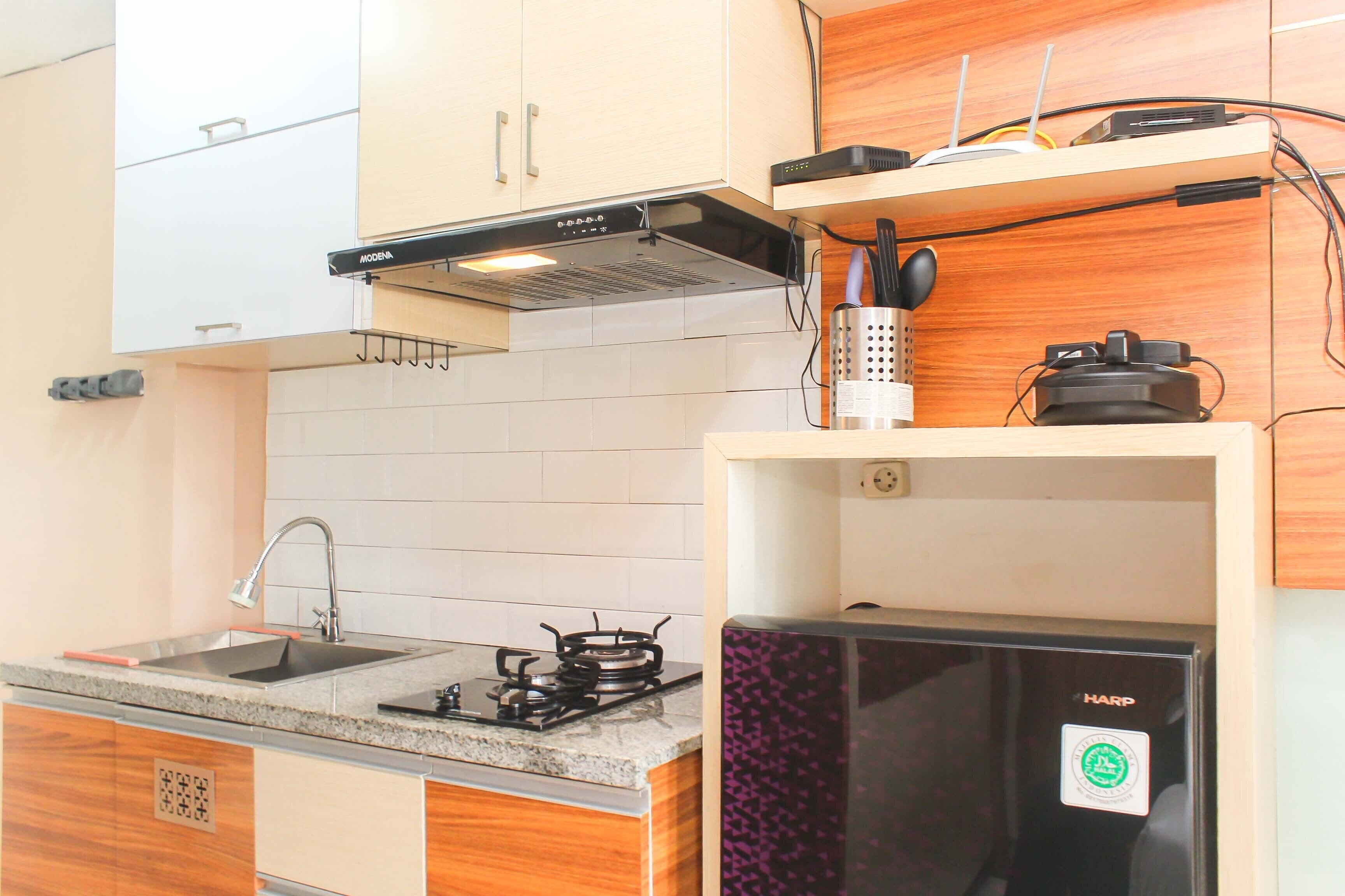 Una cocina con armarios blancos, un lavamanos de acero inoxidable, una estufa a gas y un refrigerador negro.