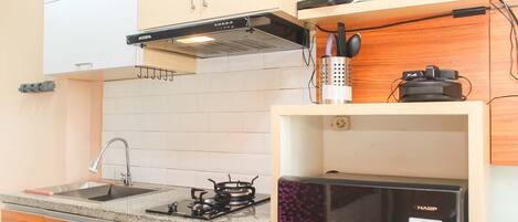 Una cocina con armarios blancos, un lavamanos de acero inoxidable, una estufa a gas y un refrigerador negro.