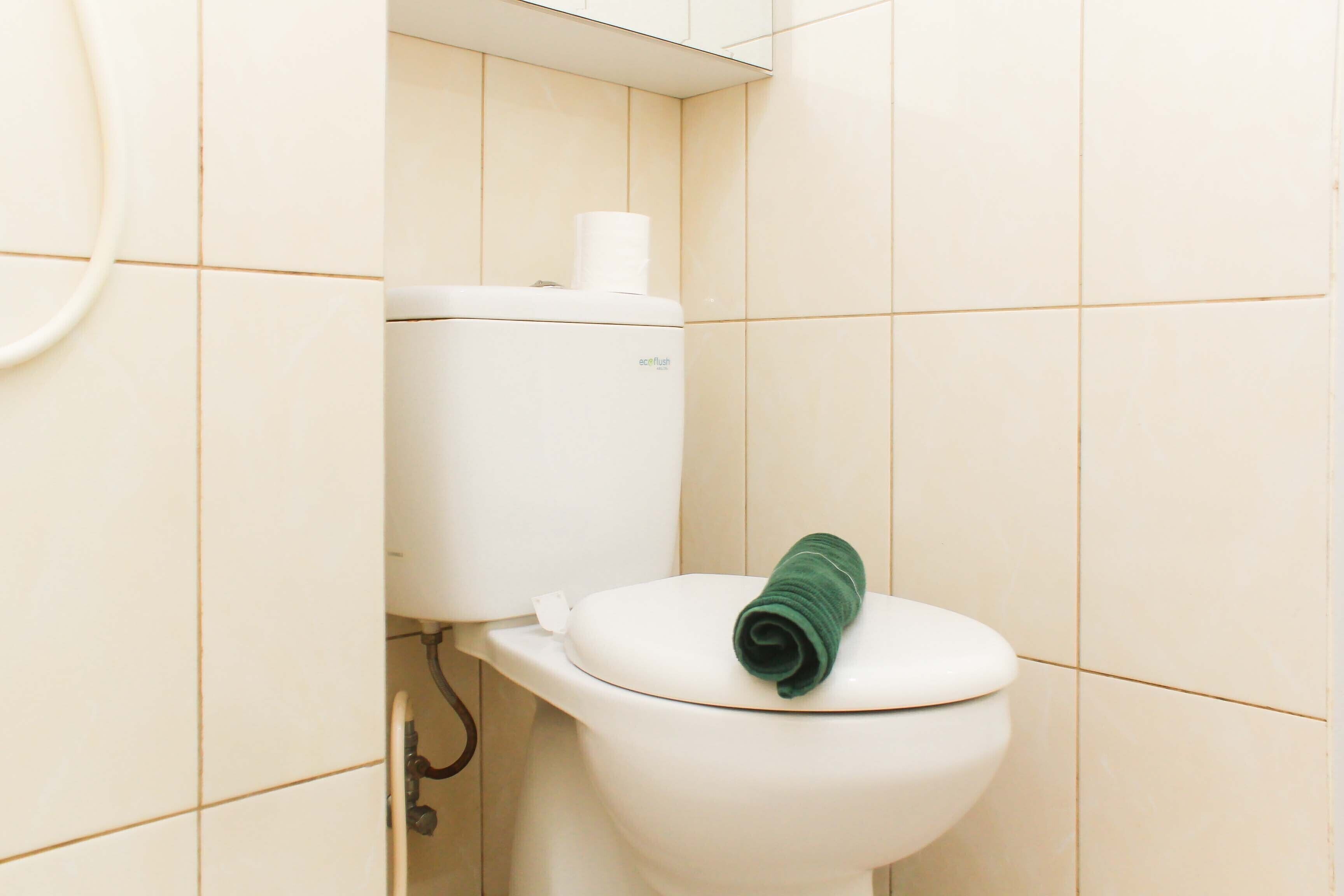 A toilet with a green towel on the seat and a toilet paper roll on the tank.