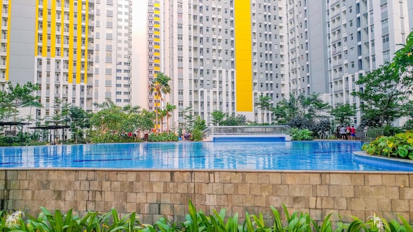 A swimming pool surrounded by greenery, with high-rise residential buildings in the background.