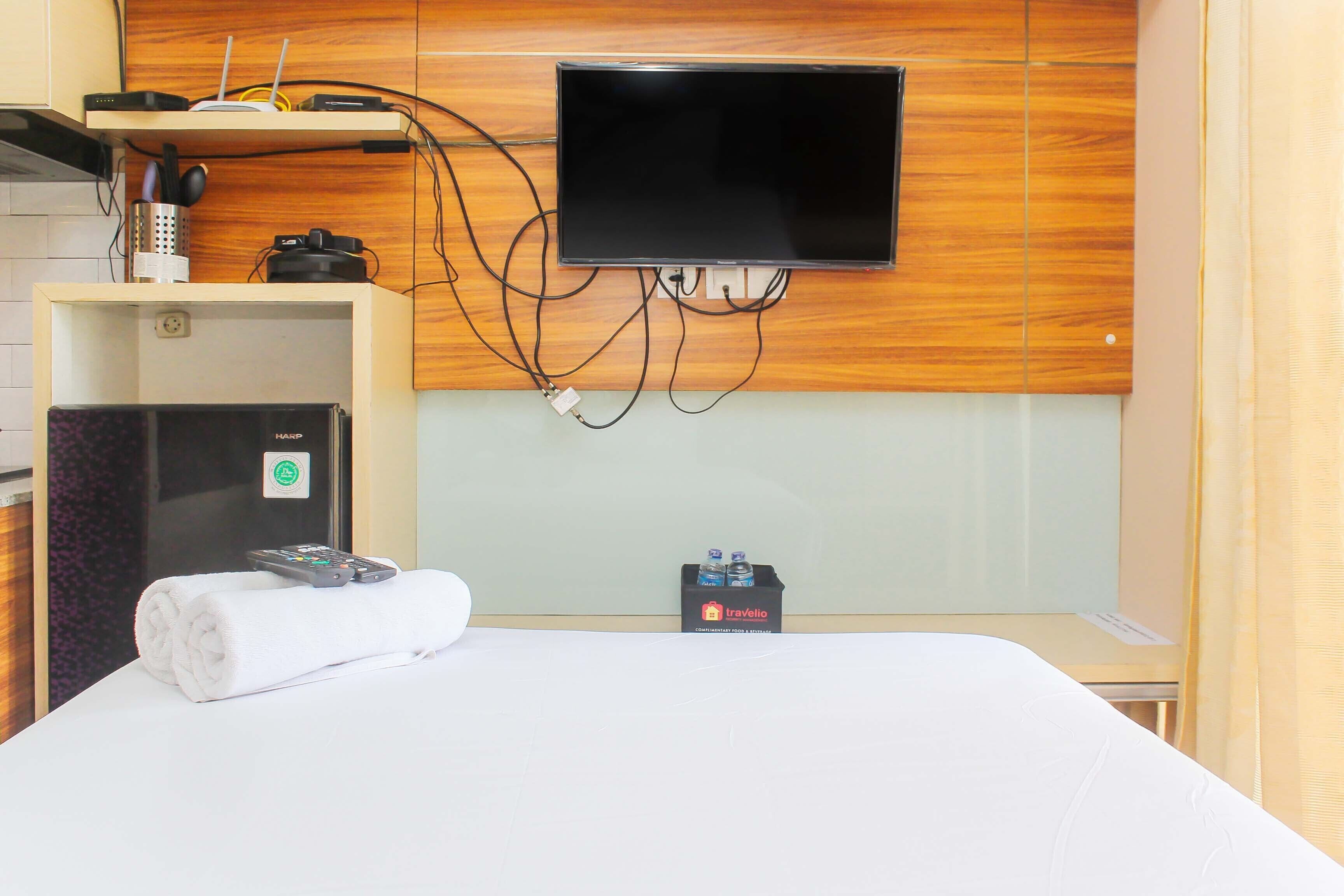 A hotel room with a bed, a TV mounted on the wall, a minibar, and a small desk.