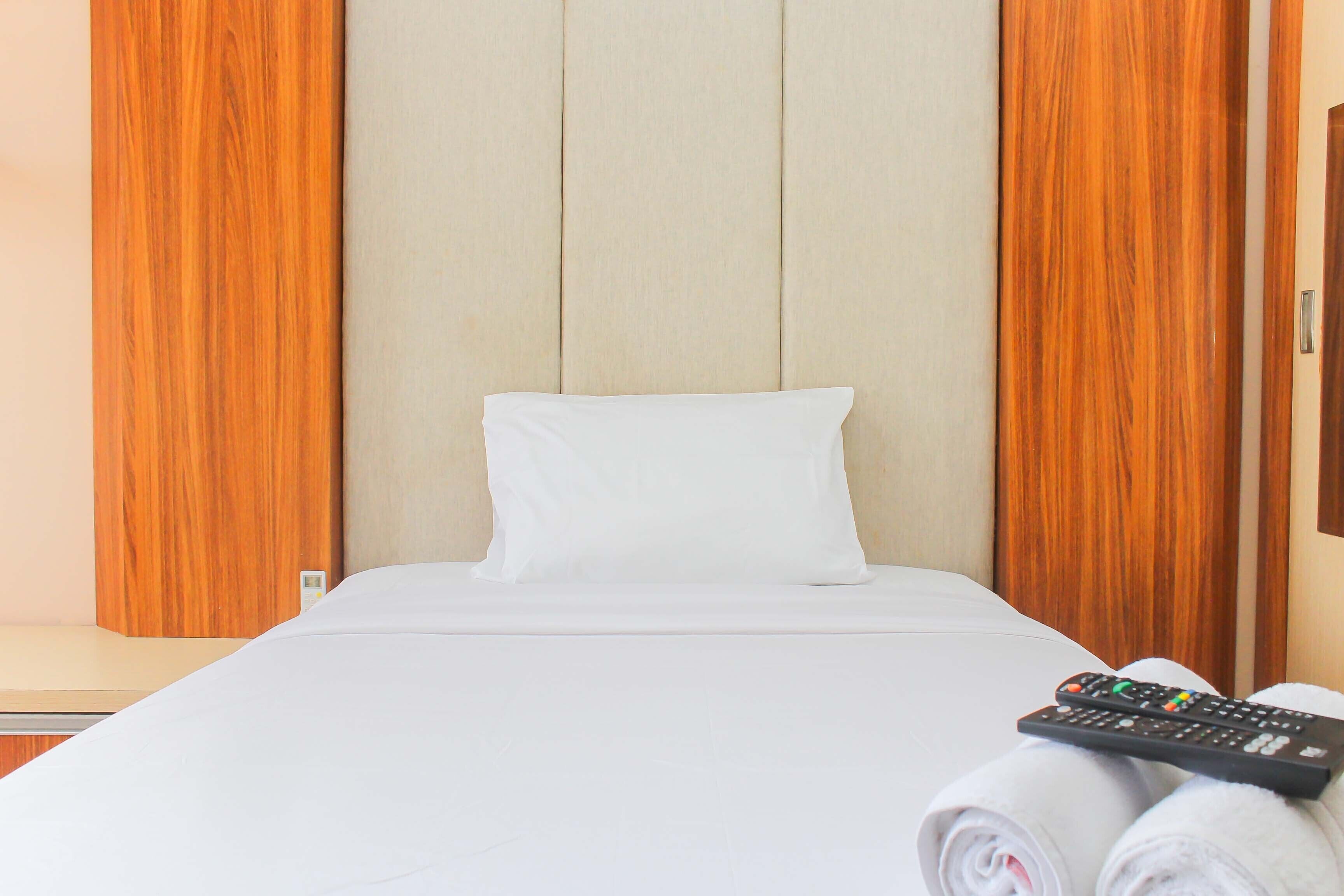 Quarto de hotel com uma cama, um travesseiro branco, uma toalha enrolada e um controle remoto.
