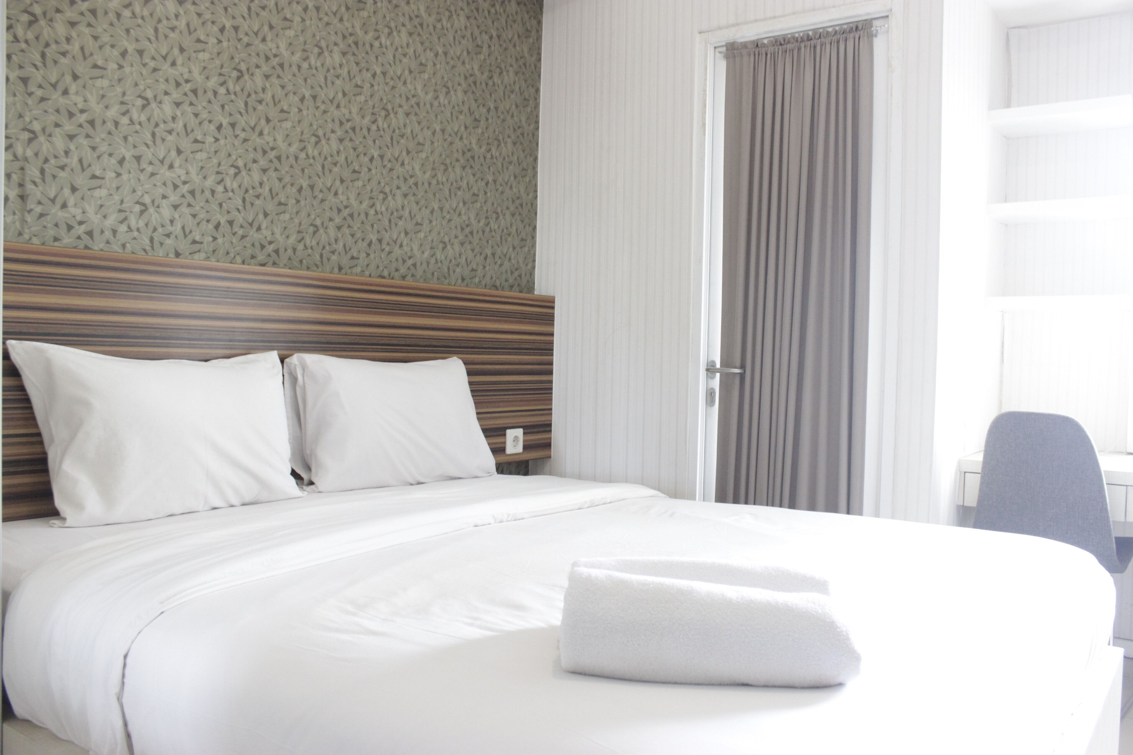 Cama bem arrumada com lençóis e almofadas brancos, cabeceira de madeira e uma toalha dobrada sobre a cama.
