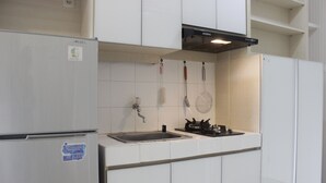 A kitchen with white cabinets, a stainless steel sink, a gas stove, and a refrigerator. - Comfy & Scenic Studio Apartment At Parahyangan Residence Near Unpar (Bandung)