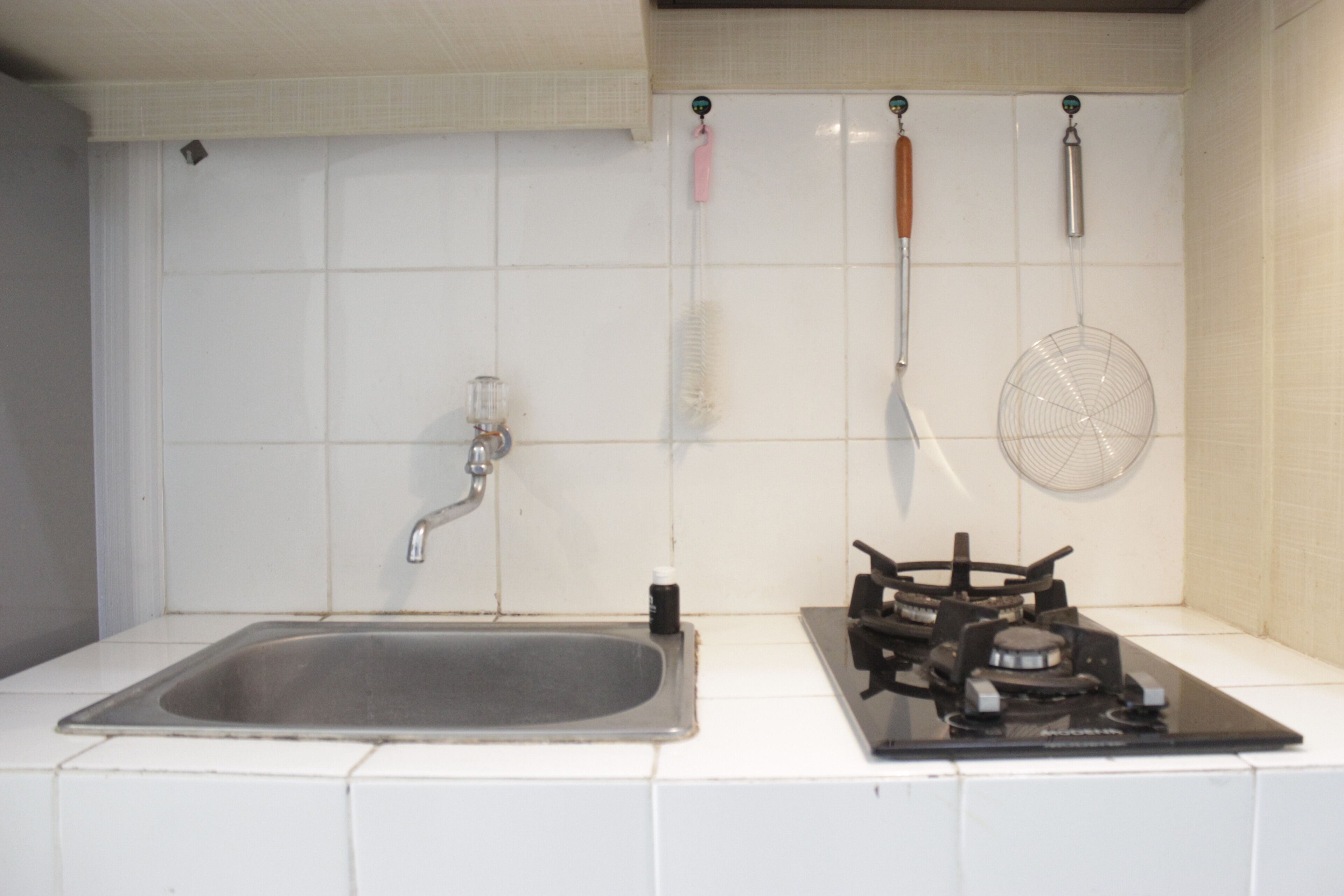 A kitchen with a sink, stove, and hanging utensils.