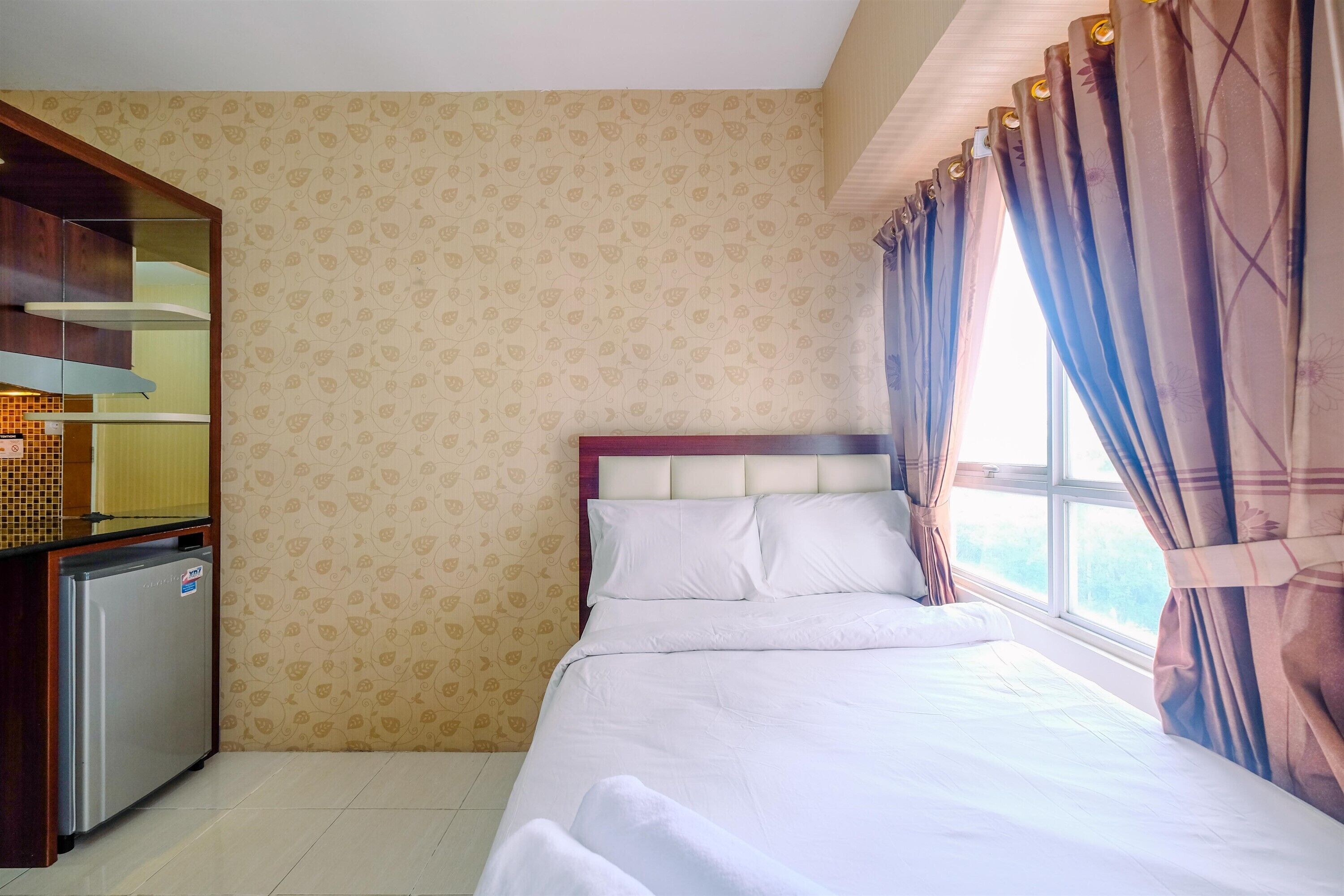 Una habitación de hotel con cama, una kitchenette pequeña y una ventana con cortinas.