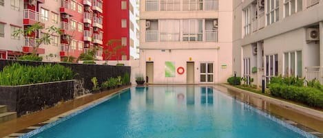 A swimming pool surrounded by multi-story residential buildings with balconies, a lifebuoy, and a sign indicating a no swimming zone.