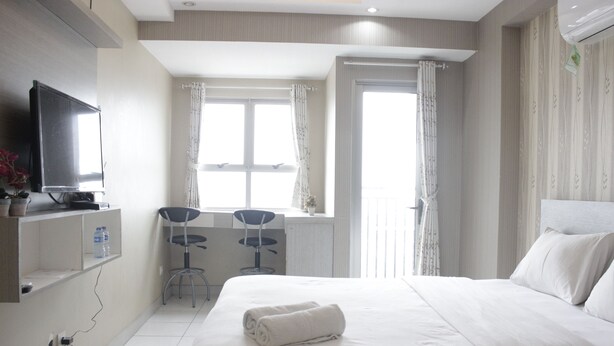 A hotel room with a bed, a TV, a desk with two chairs, and a window with curtains.