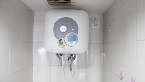 A bathroom with a white tiled wall, a white sink with a Rinnai brand label, and two pink hooks on the wall.