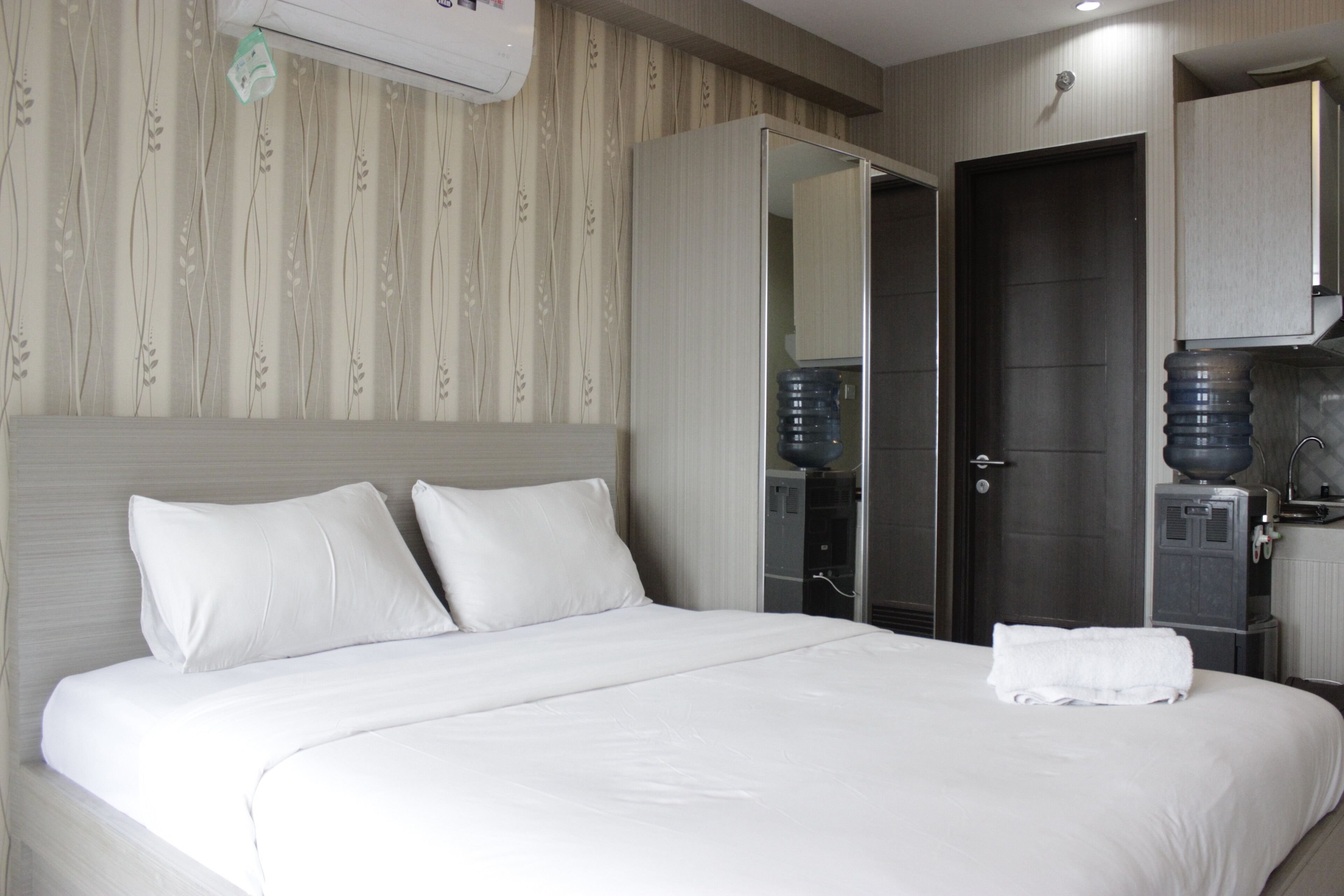 A hotel room with a large bed, a wardrobe, a water dispenser, and a mirror.
