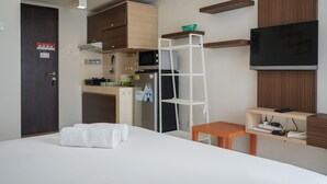 A hotel room with a bed, a TV, a kitchenette, and a wooden cabinet. - Comfortable And Simply Studio At Serpong Greenview Apartment (South Tangerang)