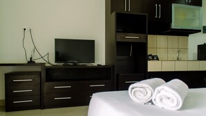 A hotel room with a bed, a TV, a desk with drawers, and a bathroom with a sink and mirror. - Elegant And Homey Studio At Paramount Skyline Apartment (Gading Serpong)