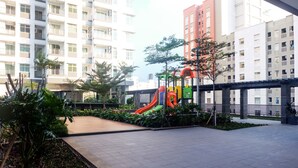 A playground area with a slide and climbing structures, surrounded by greenery and modern buildings. - Comfort And Elegant 1Br Green Bay Condominium Apartment (Jakarta)