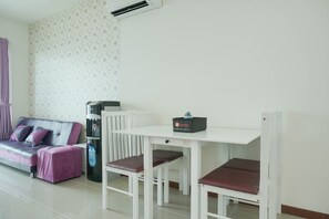 Une pièce avec un canapé blanc, une petite table et deux chaises, un distributeur d’eau et un climatiseur fixé au mur.