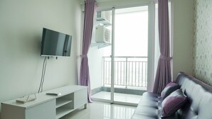 A modern living room with a flat-screen TV, a white entertainment unit, a leather sofa with cushions, and a sliding glass door leading to a balcony. - Comfort And Elegant 1Br Green Bay Condominium Apartment (Jakarta)