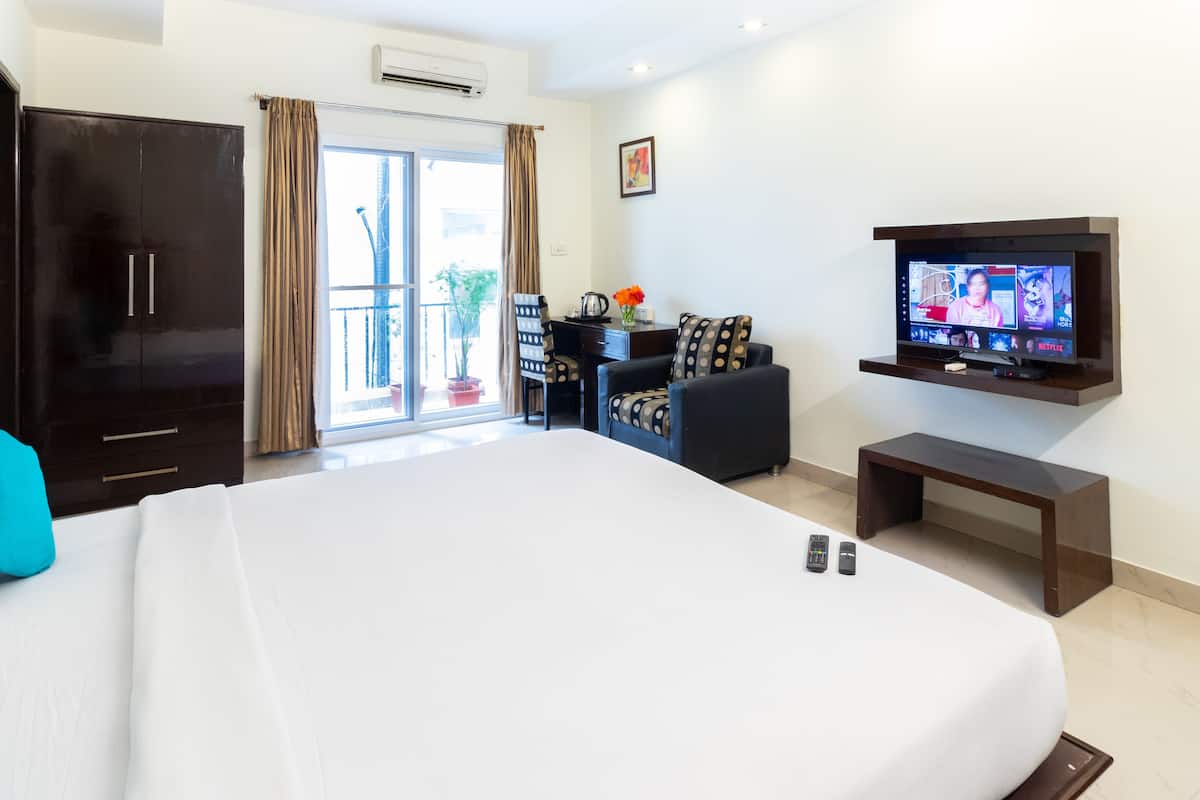 Een hotelkamer met een groot bed, een bureau met een stoel, een aan de muur bevestigde televisie en een kledingkast.