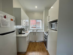 A compact kitchen with white cabinets, a built-in microwave, and a gas stove. - Summer Breeze | 2BR. Parking. Close to CBD + Beach (The Junction)