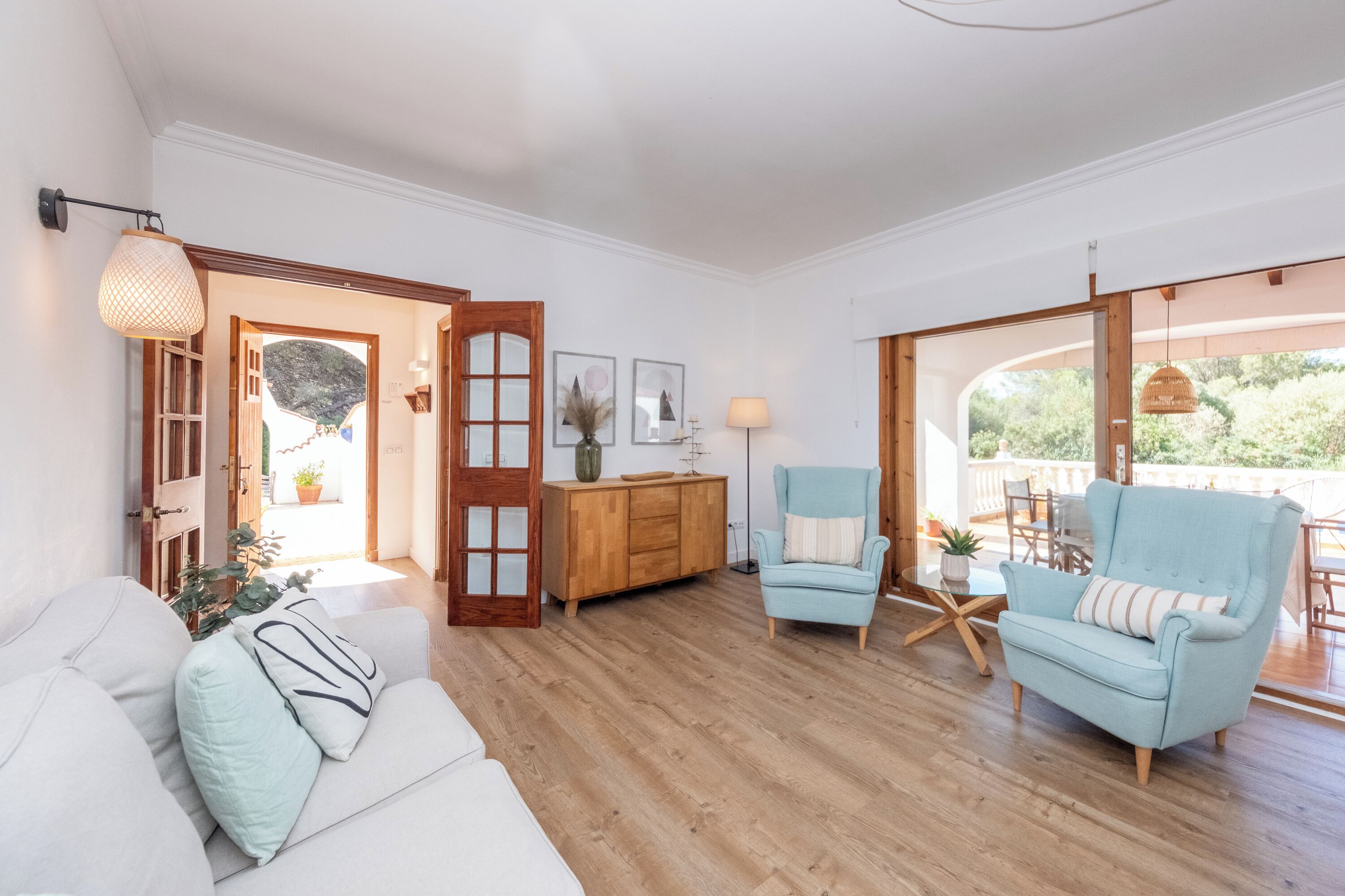A spacious living area with a wooden floor, a white sofa, a blue armchair, and a wooden cabinet.