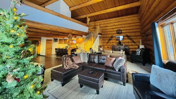 Interior espaiós d'una cabana de fusta amb un gran sostre de fusta, un arbre de Nadal, un sofà de cuir i una escala que condueix a un nivell superior.