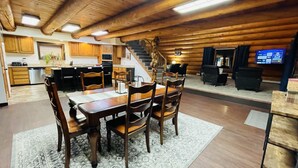 Interior espaiós d'una cabana de fusta, amb zona de dinar, cuina, sala d'estar i una escala que condueix a un nivell superior.