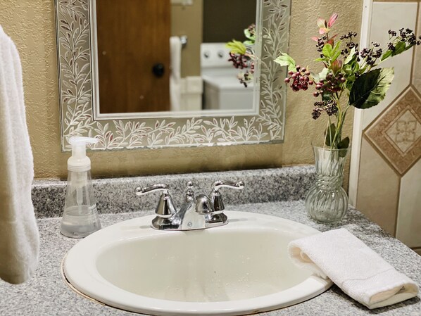 A bathroom sink with a mirror, a soap dispenser, and a vase with flowers.