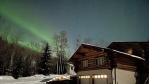 Una cabana de fusta amb un garatge, envoltada de neu i arbres.