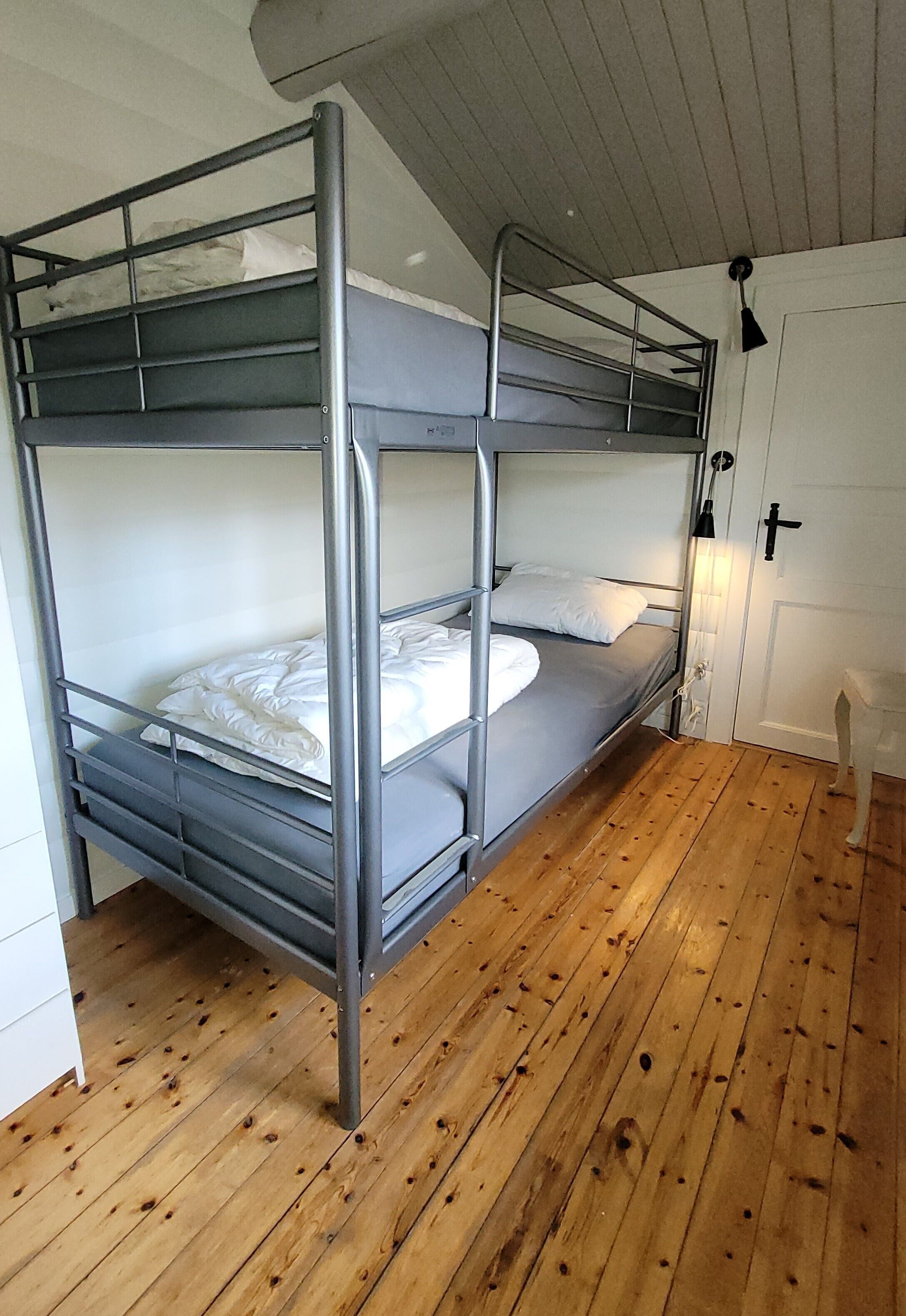 A bunk bed with metal railings in a room with wooden flooring and a white door.