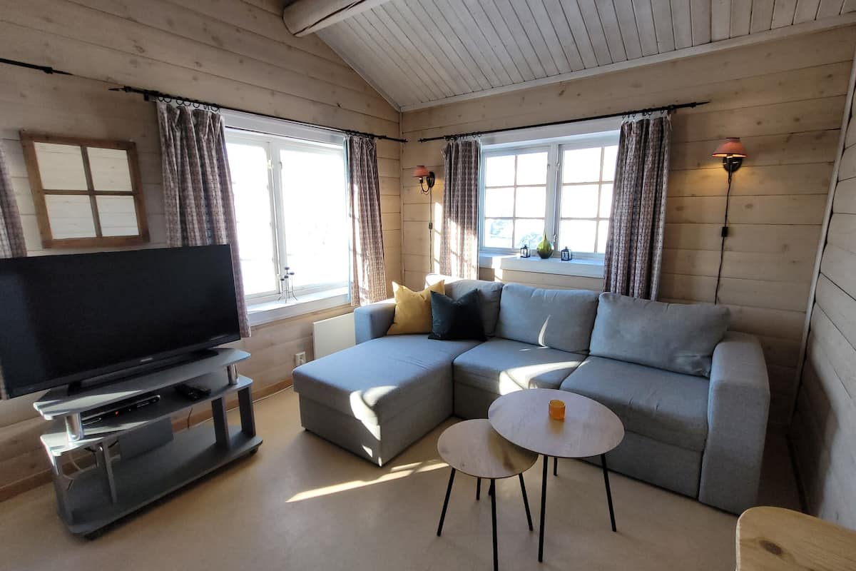 En moderne stue med en grå hjørnesofa, et fladskærms-tv, et lille rundt bord og to vægmonterede lamper.