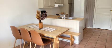 Una cocina compacta con una mesa de madera, cuatro sillas, un banco, un fregadero y un refrigerador.