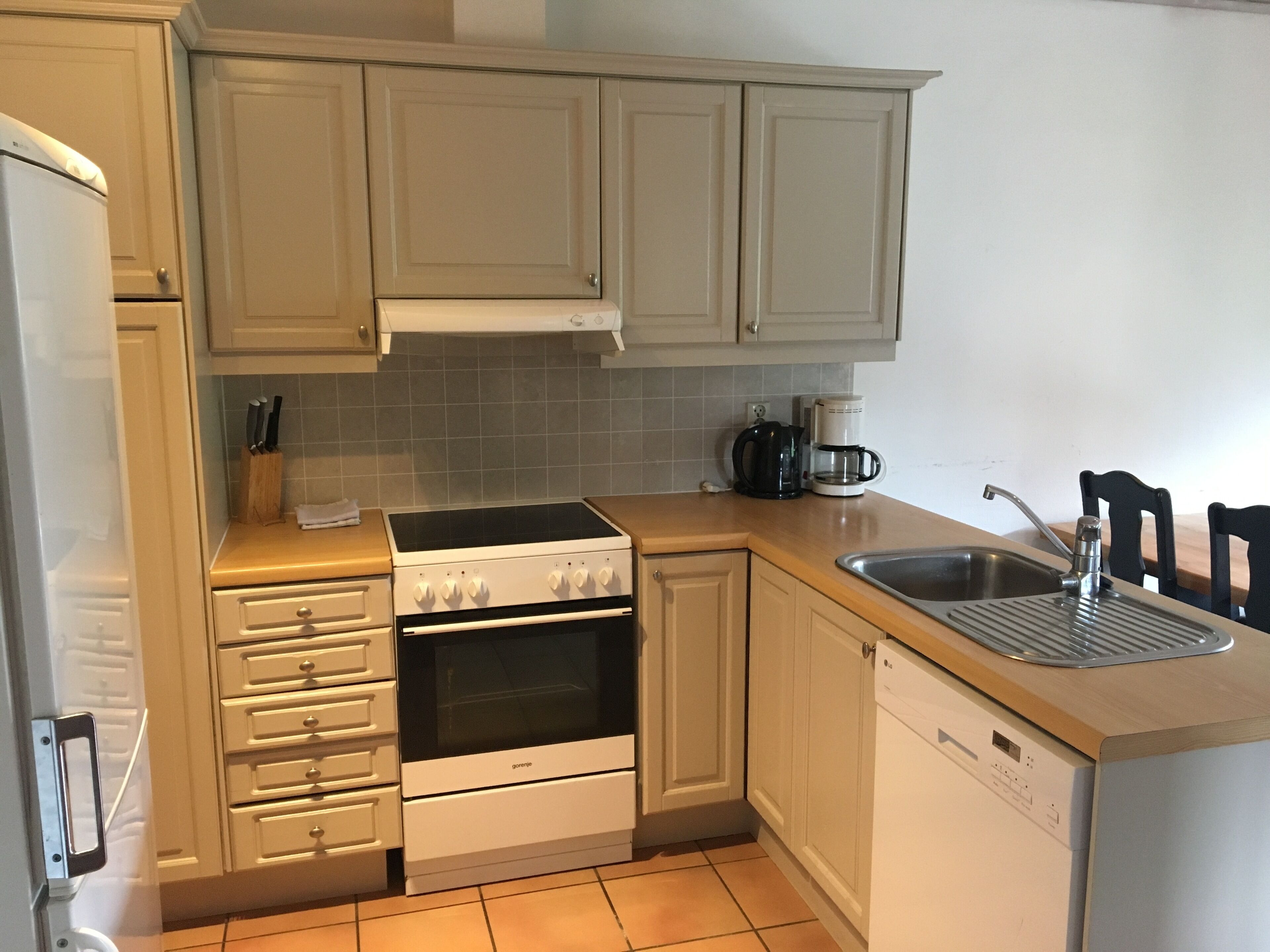 A kitchen with light-colored cabinets, a stove, a dishwasher, and a coffee maker.