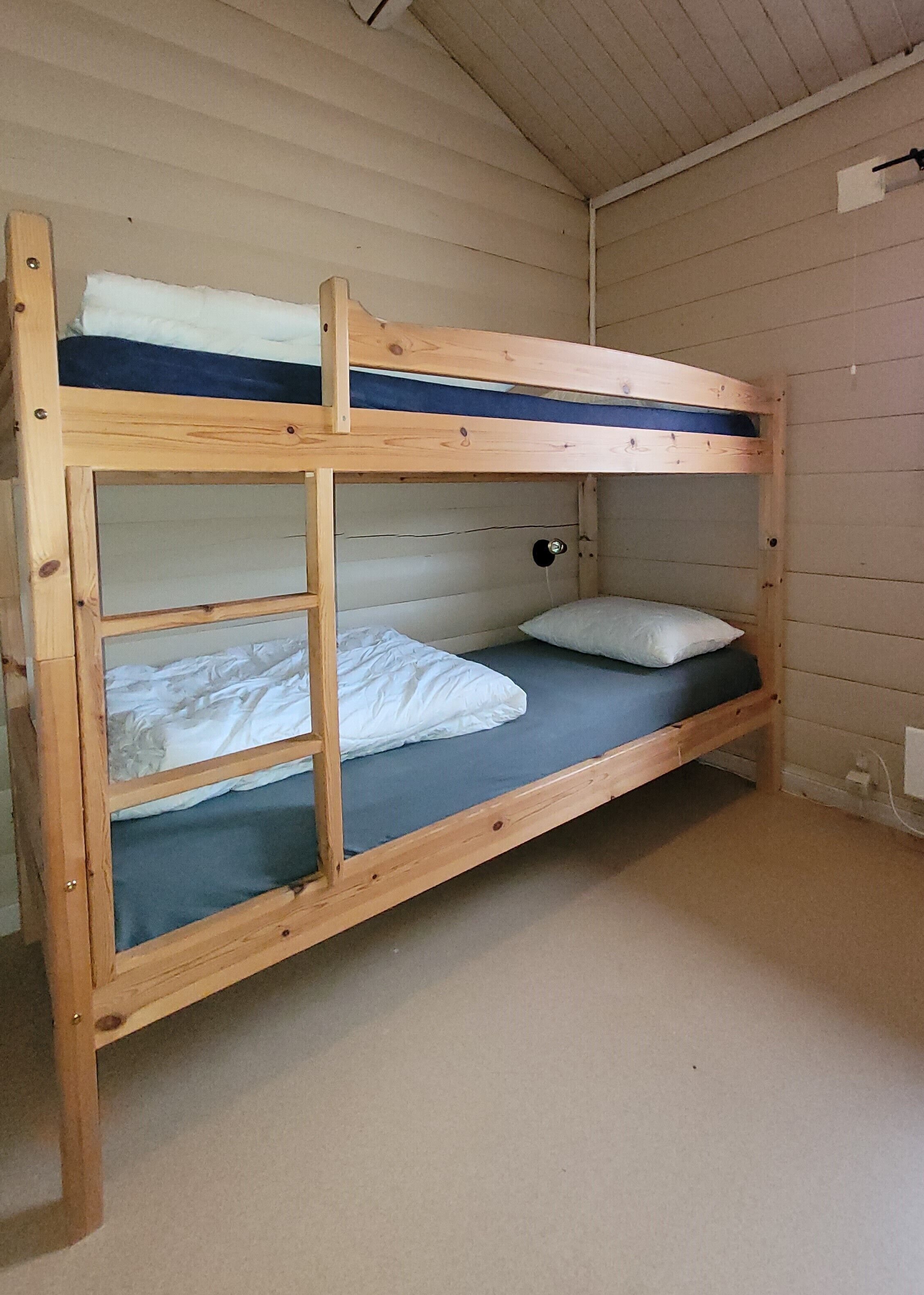 Una cama litera con estructura de madera, dos almohadas y un colchón.