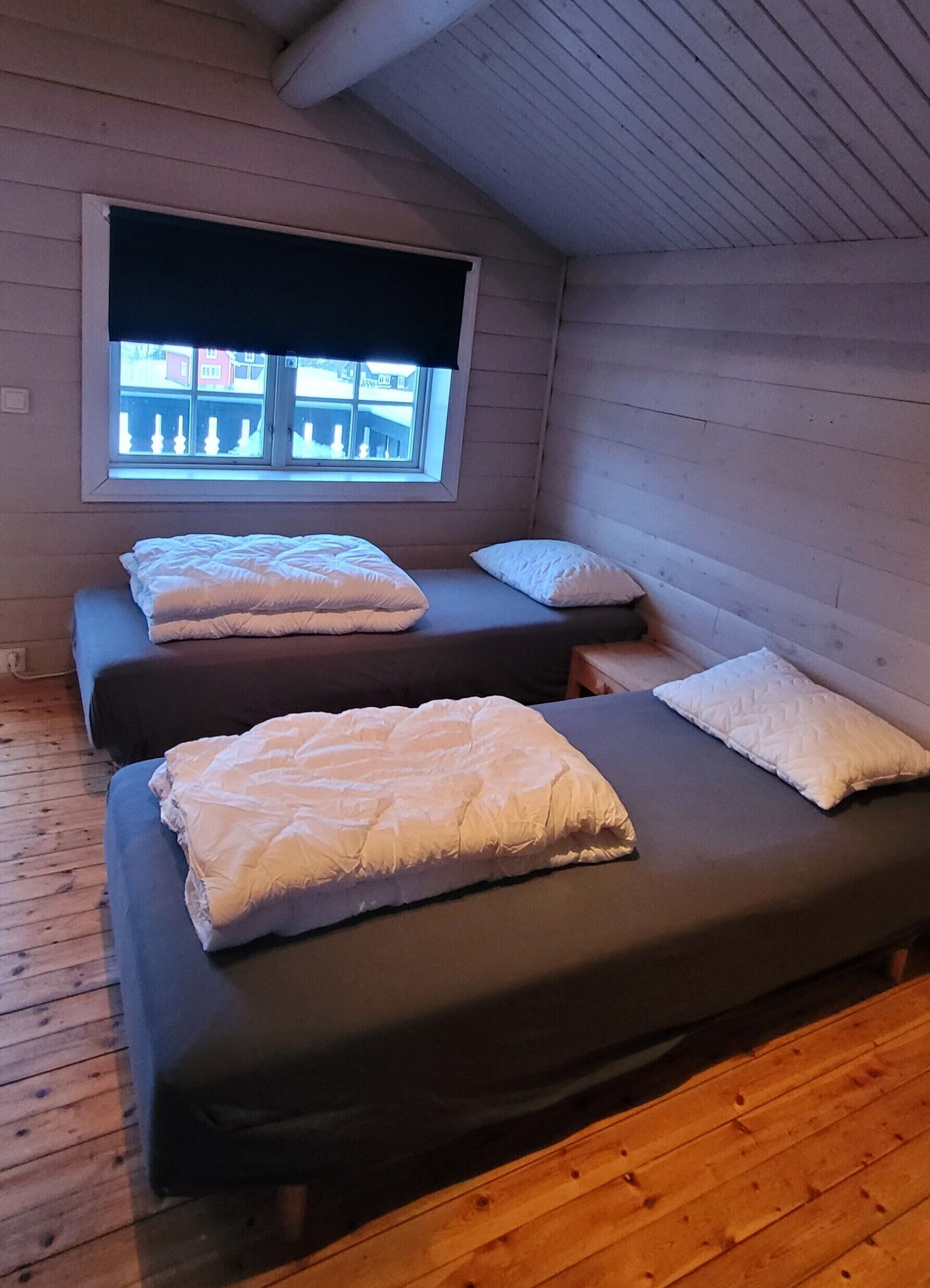 A small, cozy room with two beds, a window, and wooden walls.