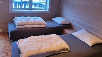 A small, cozy room with two beds, a window, and wooden walls.