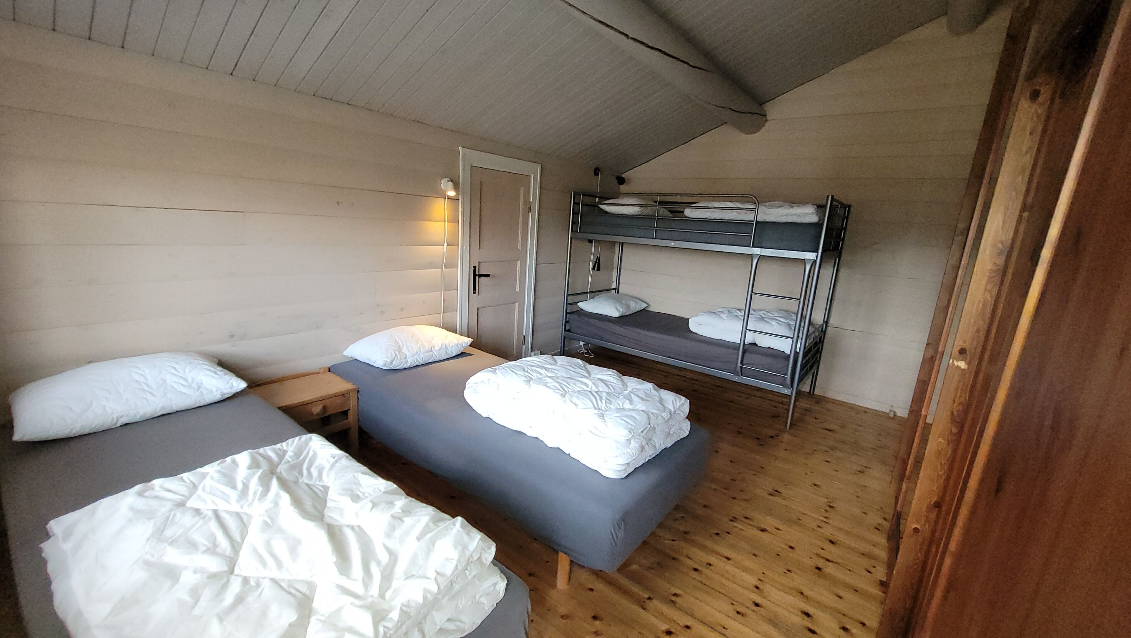 A room with two single beds, a bunk bed, wooden walls, and a door.
