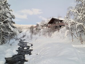 Schneebedeckte Landschaft mit einer Holzhütte und einem Fluss.