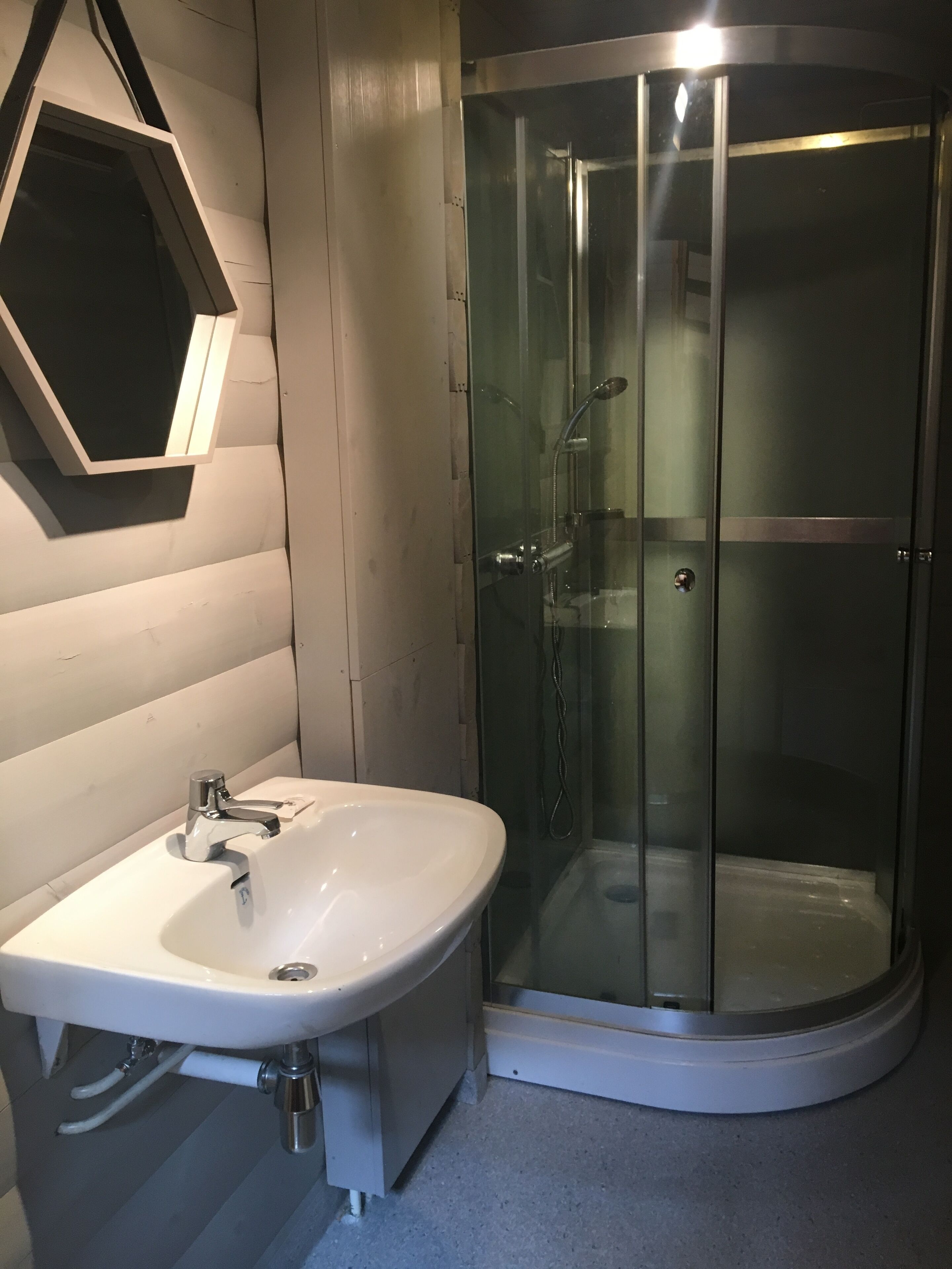 Een badkamer met een wit wastafelmeubel, een douchecabine van glas en een zeshoekige spiegel.