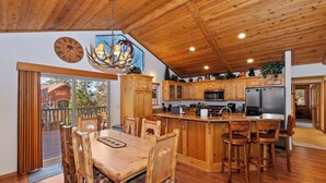A spacious kitchen with wooden cabinets, a central island with bar stools, a dining area with a wooden table and chairs, and a large window with a view of the outdoors.