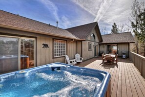 A wooden deck with a hot tub, outdoor furniture, and a covered patio area.