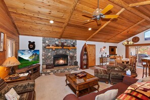 A cozy living room with a fireplace, wooden ceiling, and comfortable seating.