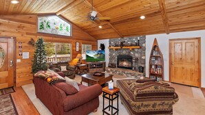 A cozy log cabin interior with a fireplace, a stone wall, a television, and a Christmas tree.