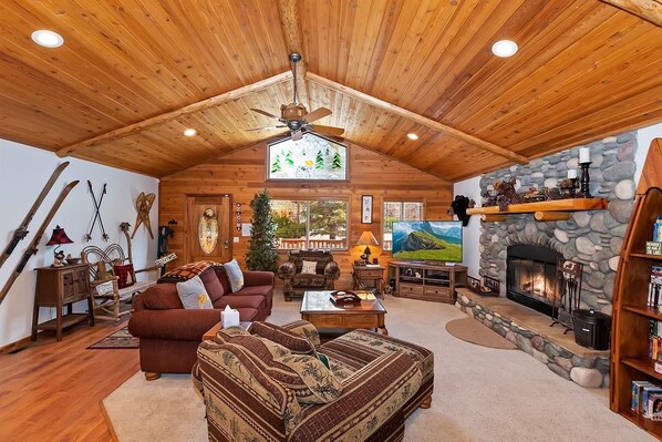 A cozy log cabin interior with a fireplace, wooden ceiling, and a stone wall.