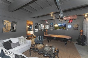 Une pièce comprenant une table de billard, un canapé, une table basse et divers éléments de décoration murale, notamment des tableaux encadrés et un jeu de fléchettes.