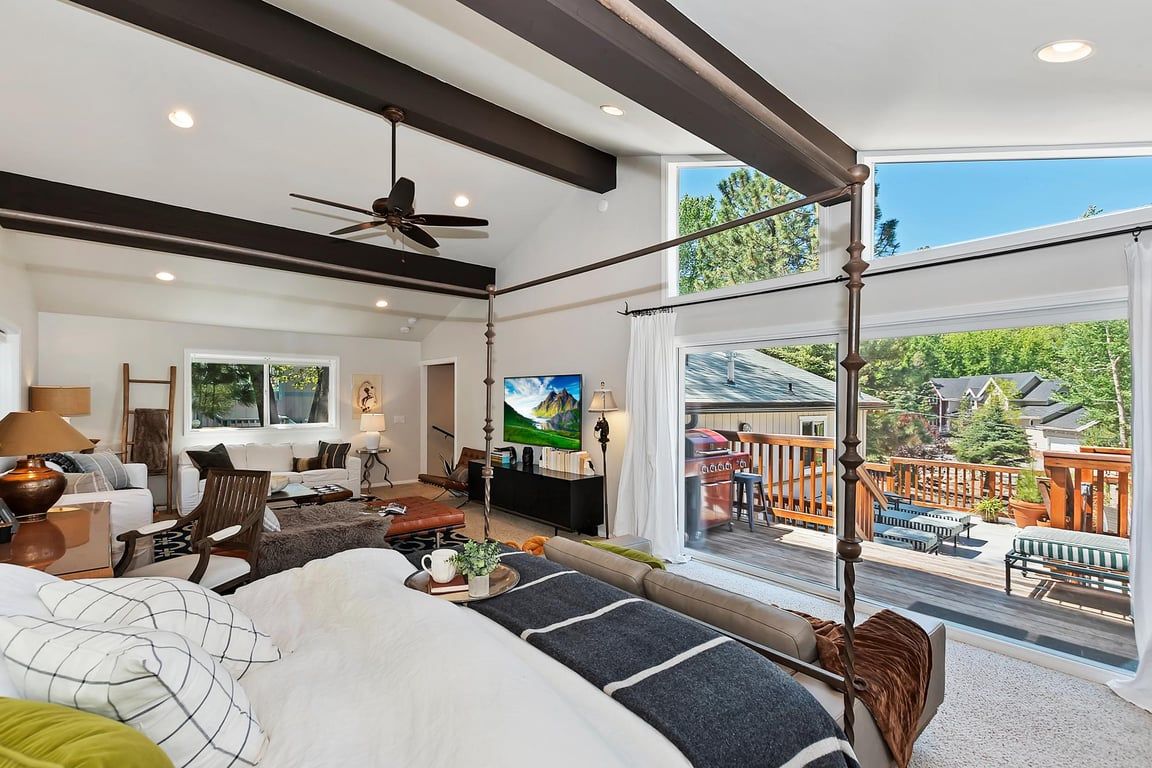 A spacious bedroom with a large bed, a ceiling fan, and a balcony with a view of the outdoors.